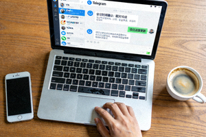 从上方俯拍的工作桌场景，一台打开的笔记本电脑显示着Telegram的中文聊天界面，旁边放着手机和咖啡